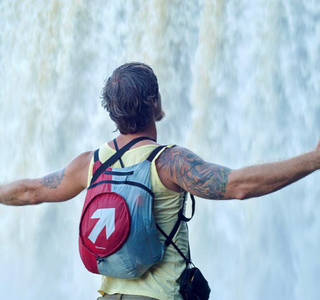 A backpacker captivated by nature's beauty, standing before a majestic waterfall. The perfect adventure awaits!