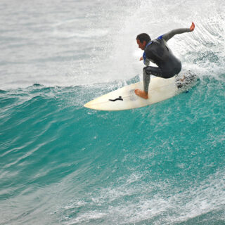 A man skillfully rides a wave on a surfboard, displaying his balance and control amidst the crashing water.